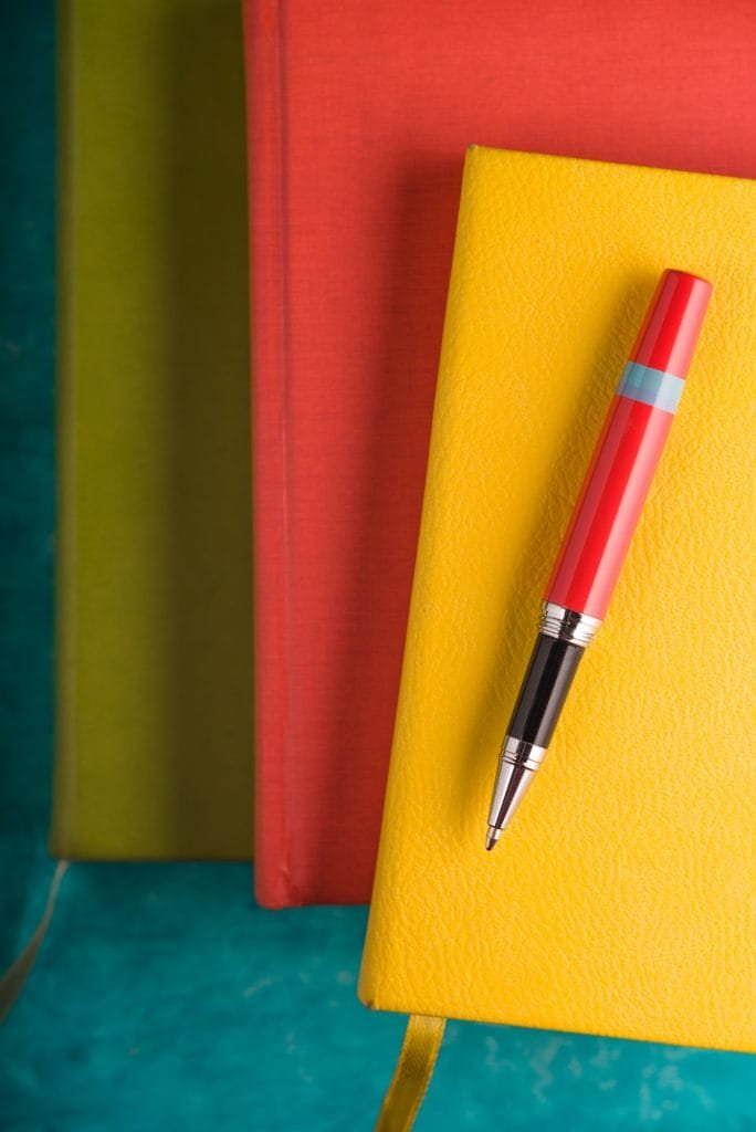 Värikkäitä vihkoja ja kynä