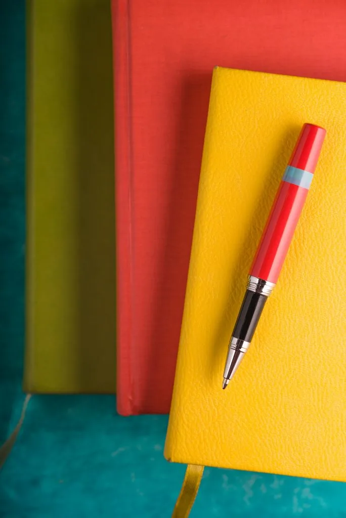 Värikkäitä vihkoja ja kynä