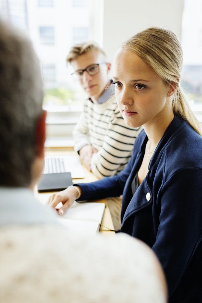 Naisoppilas kuuntelee opettajaa istuessaan kokoushuoneessa